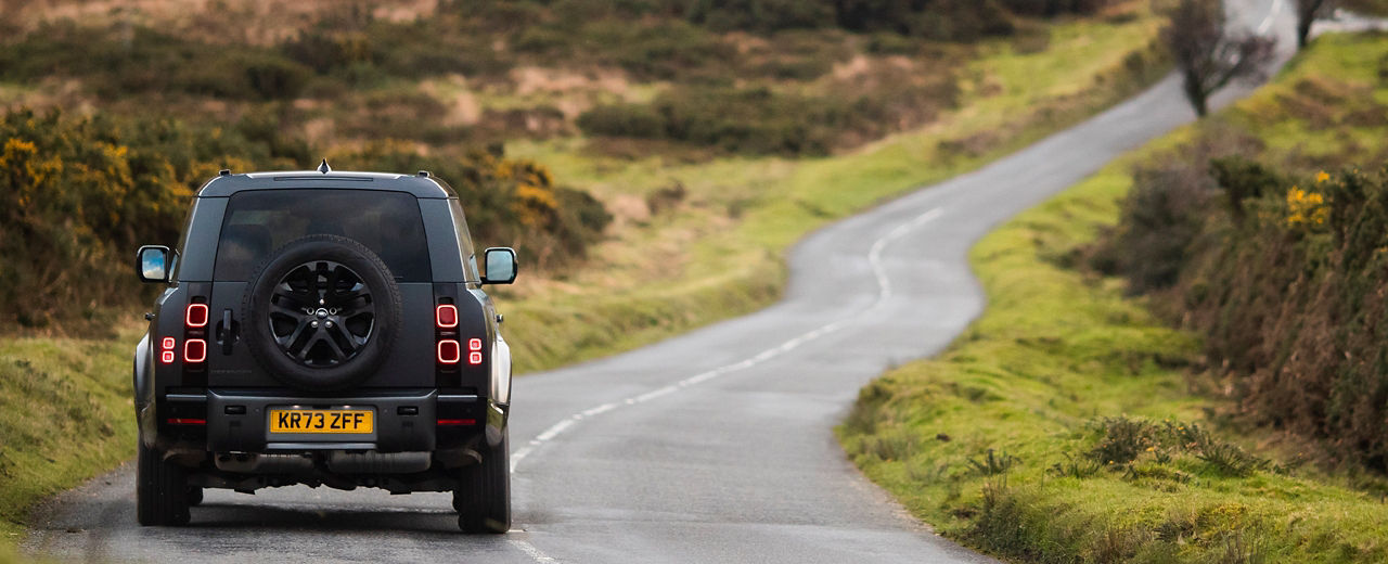 A Defender drives along a country road, turning a slight corner