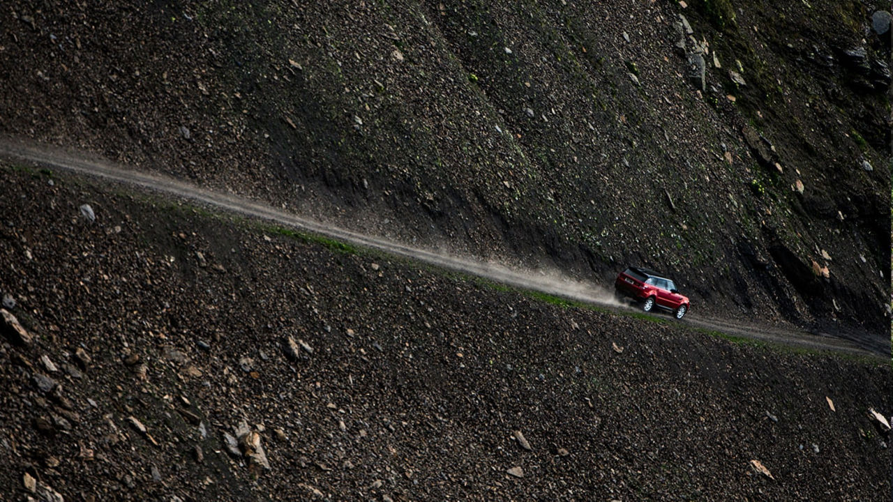 Range Rover in red driving a rock road on a mountain