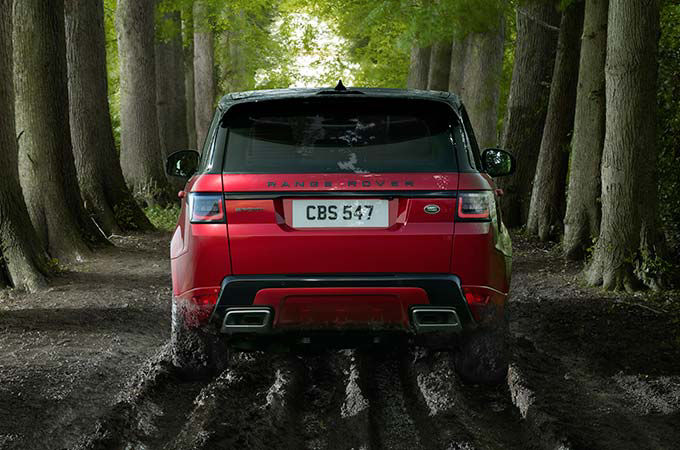 Range Rover Sport in red driving in forest back view