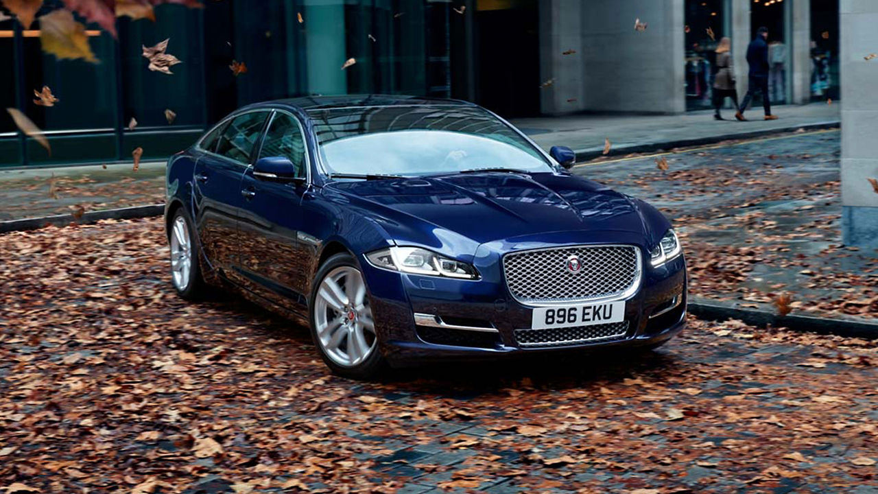 Jaguar XJ running on city road covered with leaves