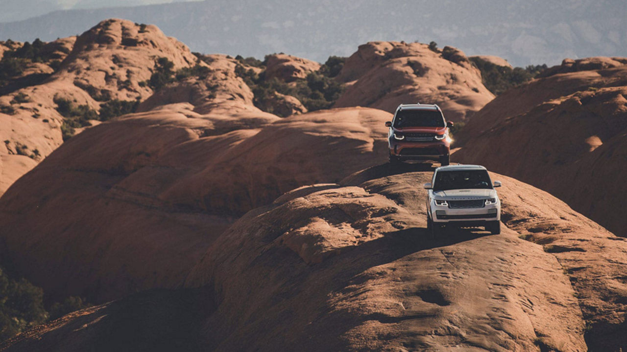 Land Rover Discovery vehicles driving on a rock in a desert background