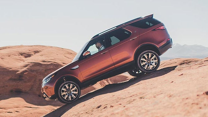 Land Rover Discovery in orange parked on a rock profile view