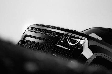 Close-up of a black Defender SUV front grille and LED headlight, highlighting rugged design details against a minimalist studio backdrop.