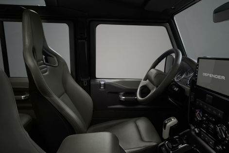 Minimalist Defender interior featuring sculpted front seats, a multifunction steering wheel, rugged controls, and a large touchscreen display.