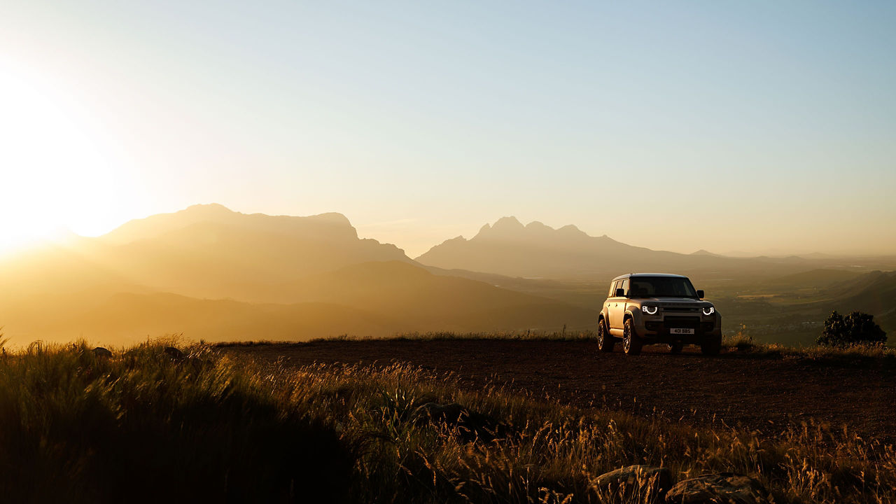Defender Octa driving in a field under the sunset