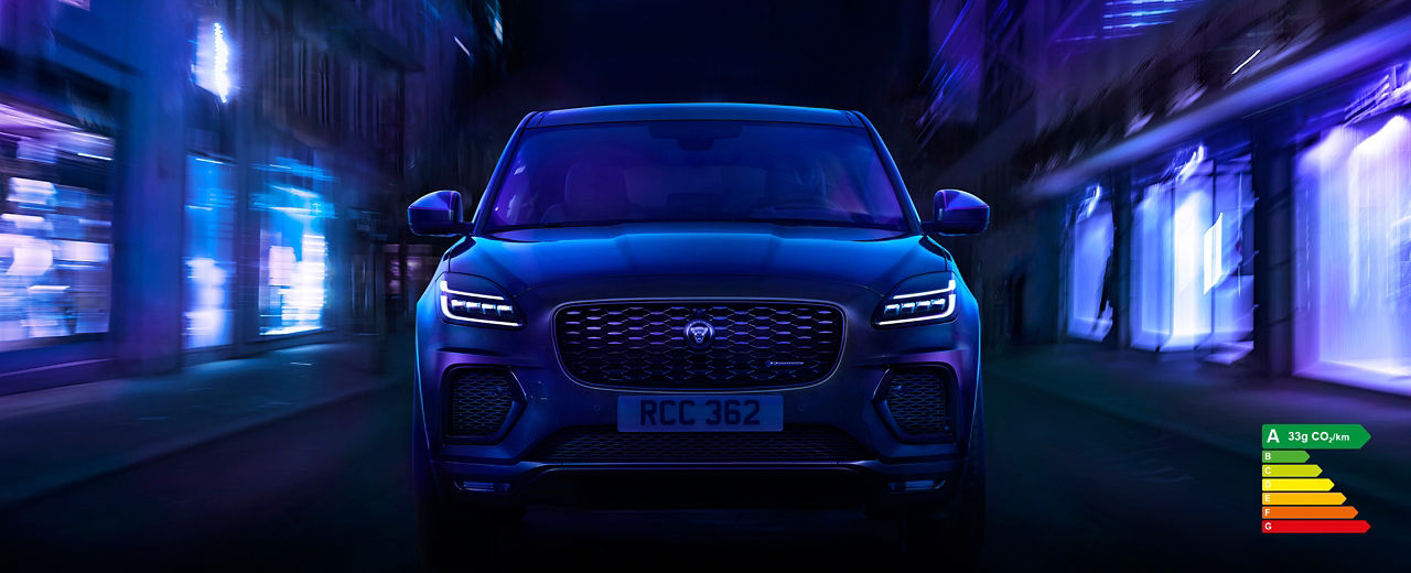 E-PACE driving through the city at night with energy efficiency label A (33g CO2/km).