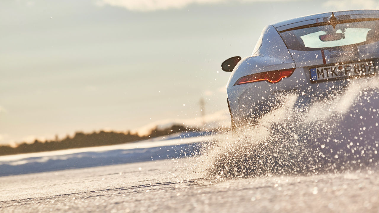 Jaguar car passes through a snowdrift and snowy land road at winter