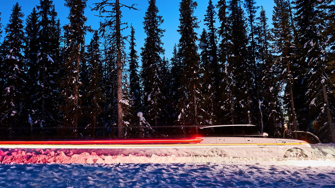 Range Rover light trails on a snowy winding road in Lapland with snowy trees background