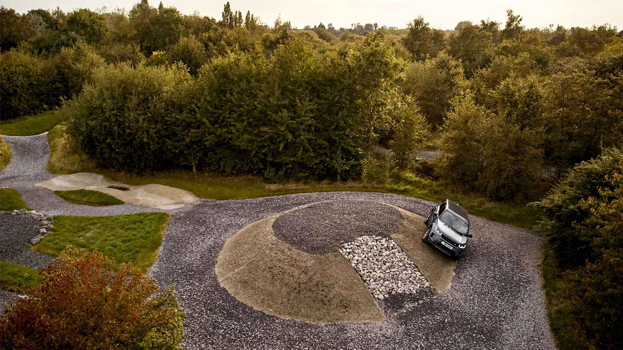 Top view of an Discovery driving on a circular gravel track surrounded by trees.