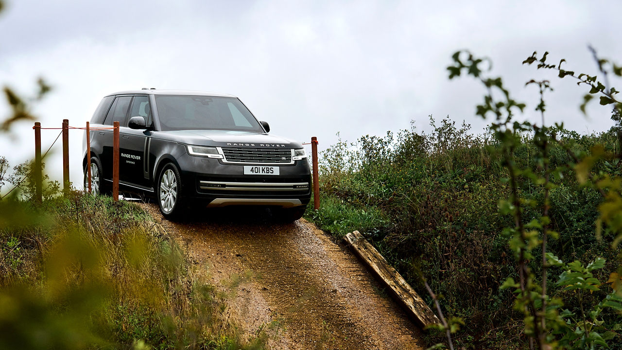 Black Range Rover on a narrow dirt path surrounded by greenery.