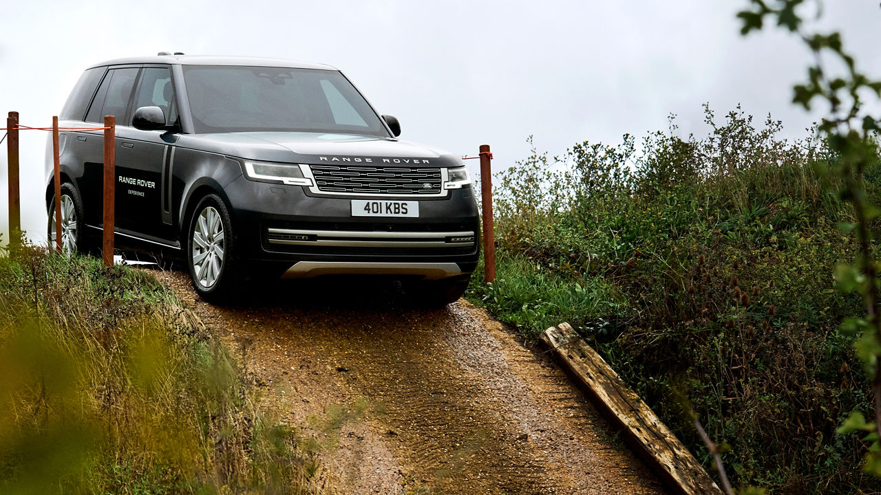 Black Range Rover on a narrow dirt path surrounded by greenery.