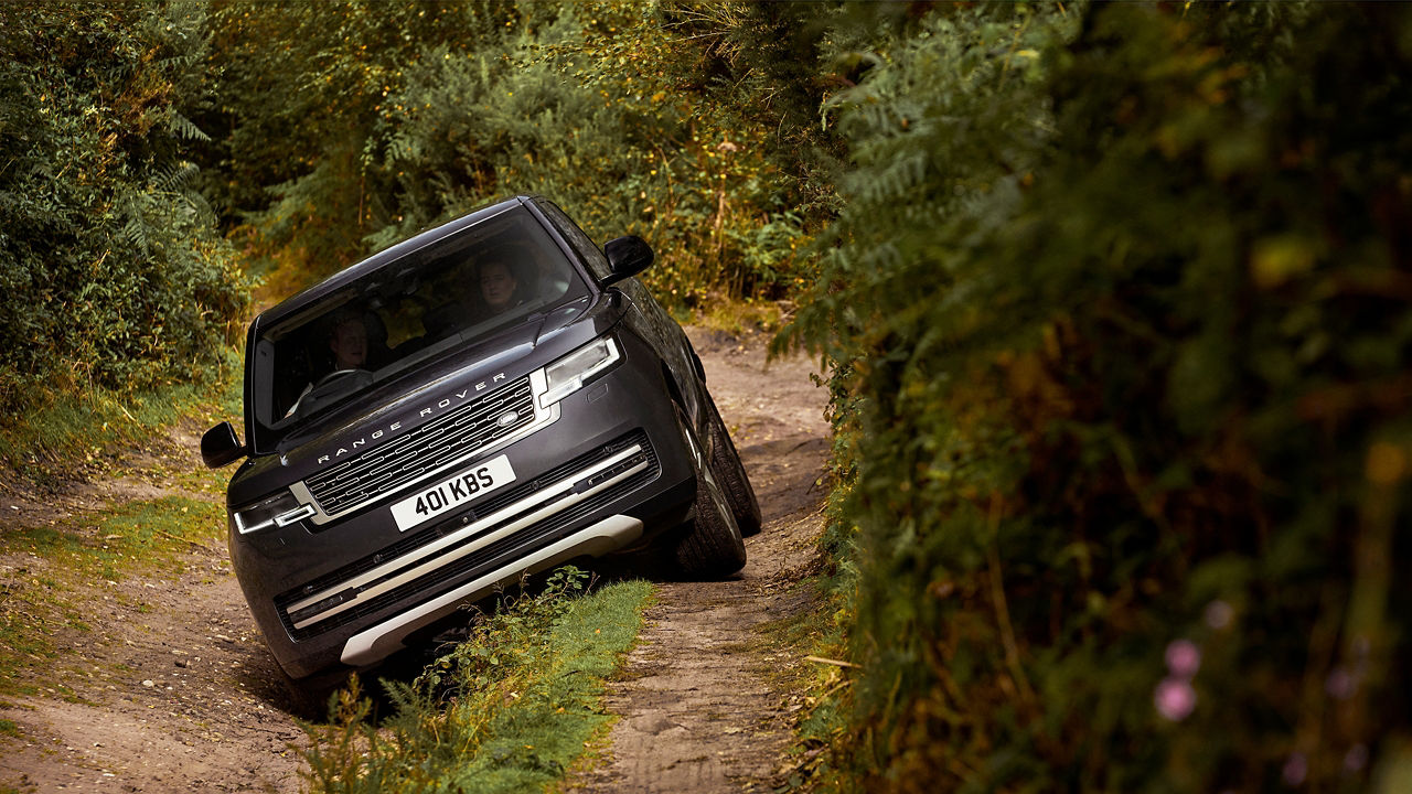 Black Range Rover driving off-road on a Narrow dirt track surrounded by greenery.