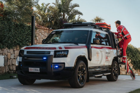 White emergency response SUV with red safety markings parked outdoors, with a responder standing on a side step accessing roof-mounted equipment.