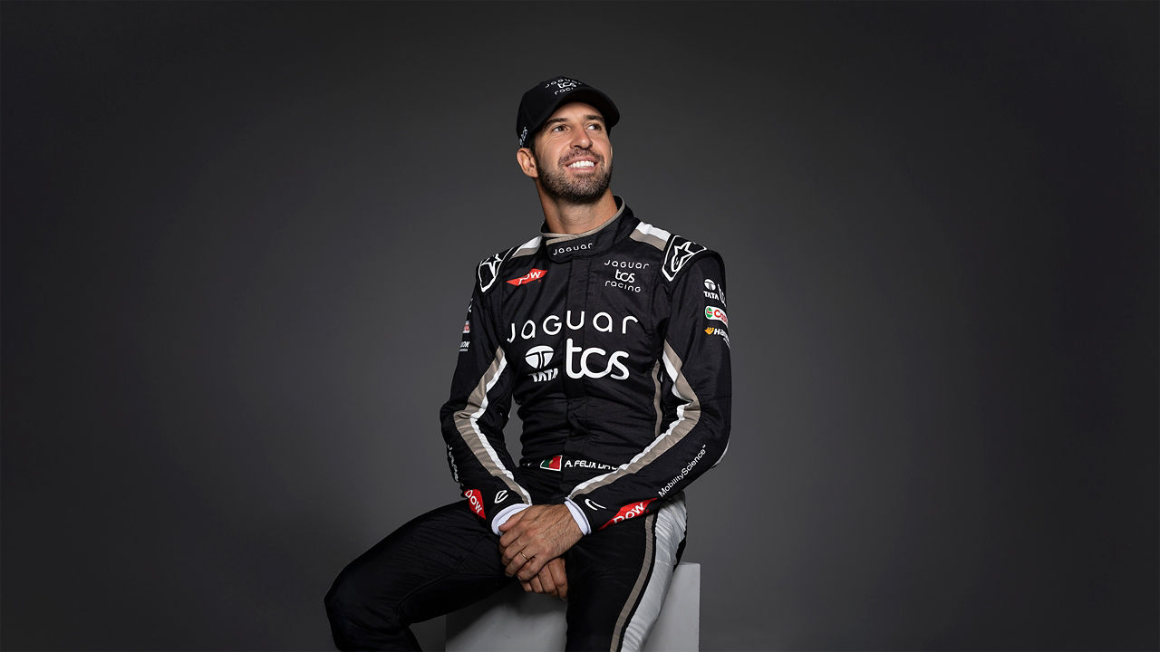 A racing driver in a Jaguar TCS suit sits on a box posing for a studio photo.