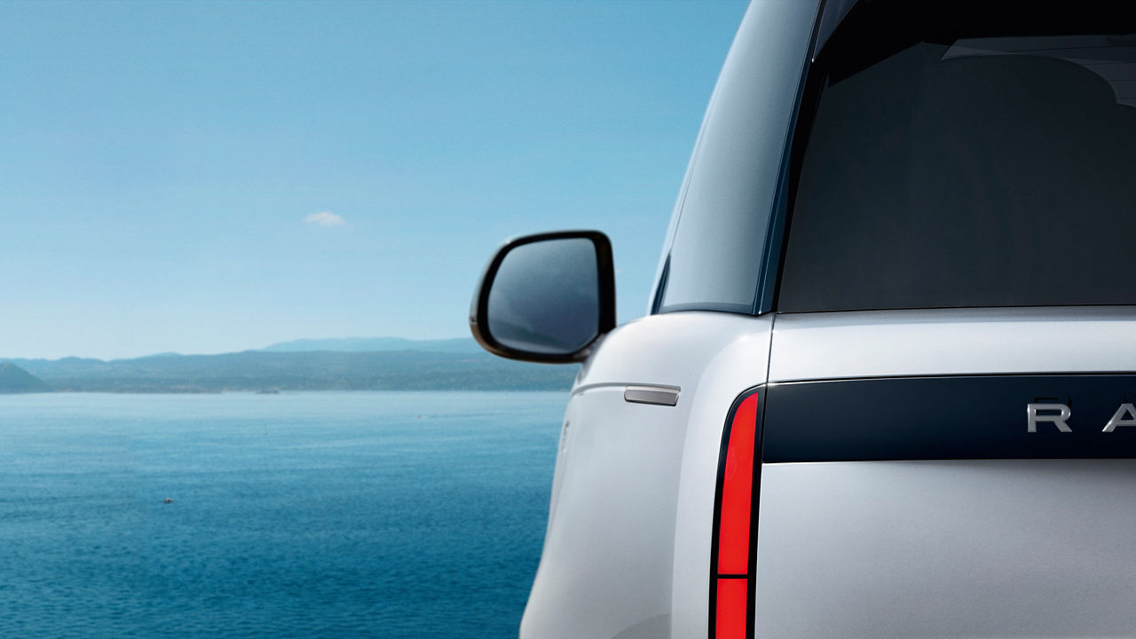 Rear side view of a White Range Rover parked near a body of water.