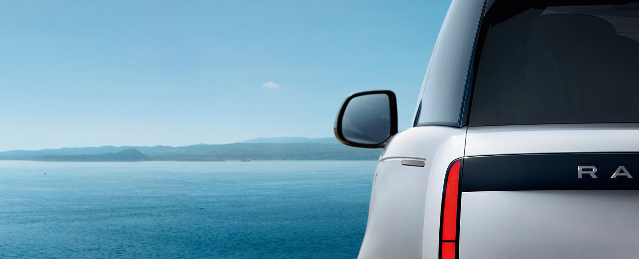 Rear side view of a White Range Rover parked near a body of water.