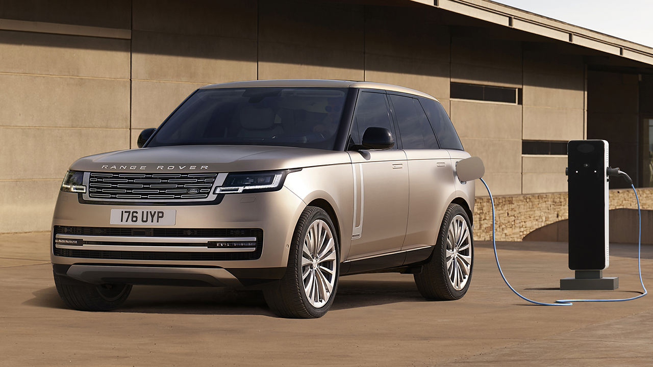 Range Rover PHEV in Corinthian Bronze plugged into a charging station in front of a building.