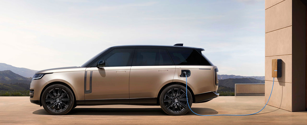 Range Rover PHEV in Corinthian Bronze plugged into a charging station next to building.