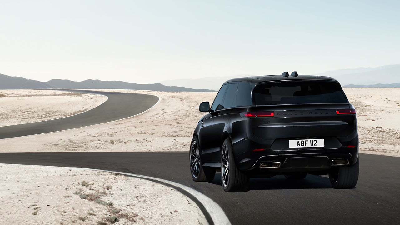 A Range Rover Sport in Santorini black turning a corner on a road out in the desert