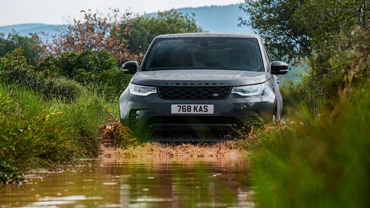 Discovery driving through shallow water on a grassy trail.