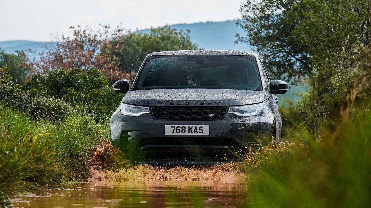 Discovery driving through shallow water on a grassy trail.