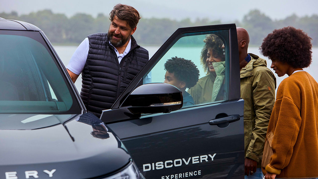 People standing next to a Discovery with the front door open, talking outdoors.