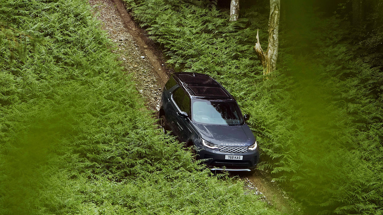 Black Discovery driving through a narrow green forest trail.