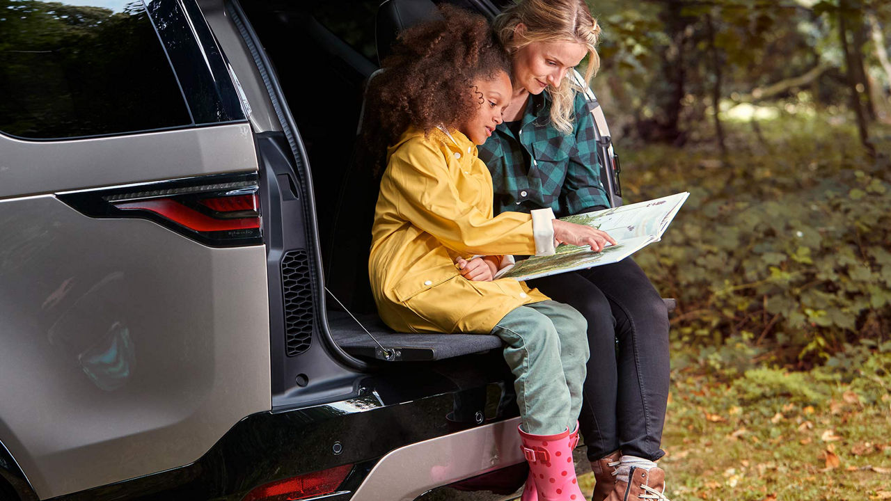 A woman and child sitting on the boot of a discovery