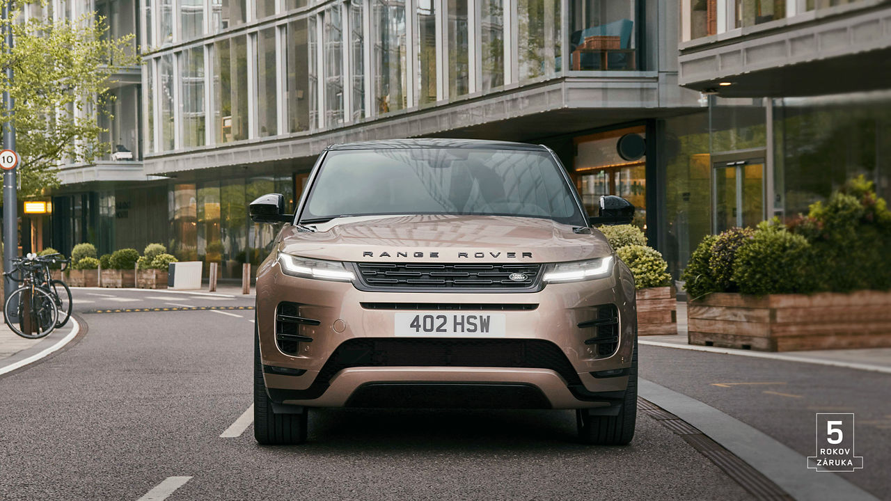 Front view of Range Rover Evoque in Corinthian Bronze driving through the streets of a city with 5 years warranty watermark.