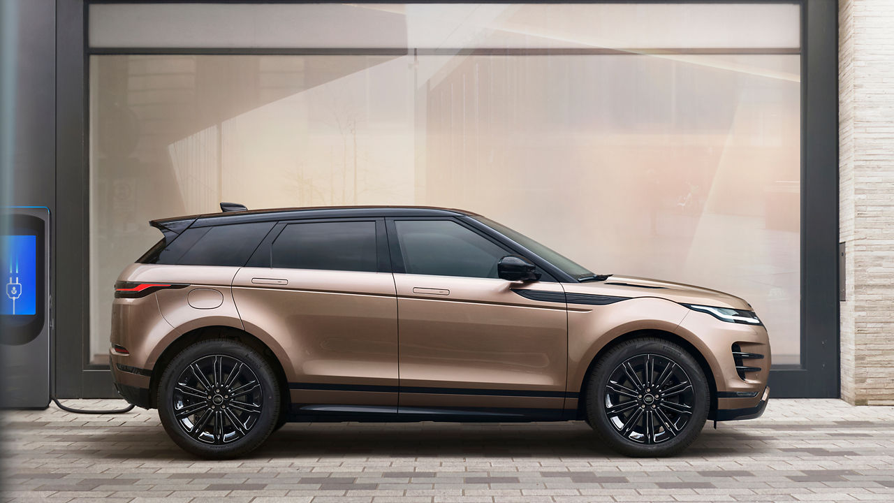 Range Rover Evoque PHEV in Corinthian Bronze plugged into a charging station in front of a building.