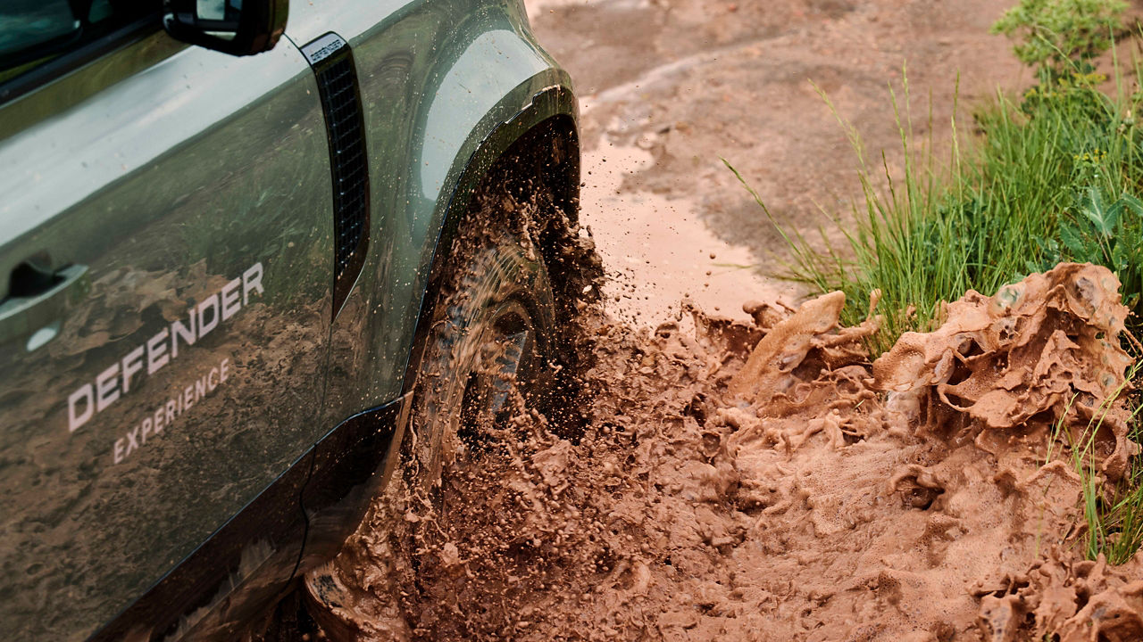Close-up of a Defender wheel splashing through mud on n off-road trail.