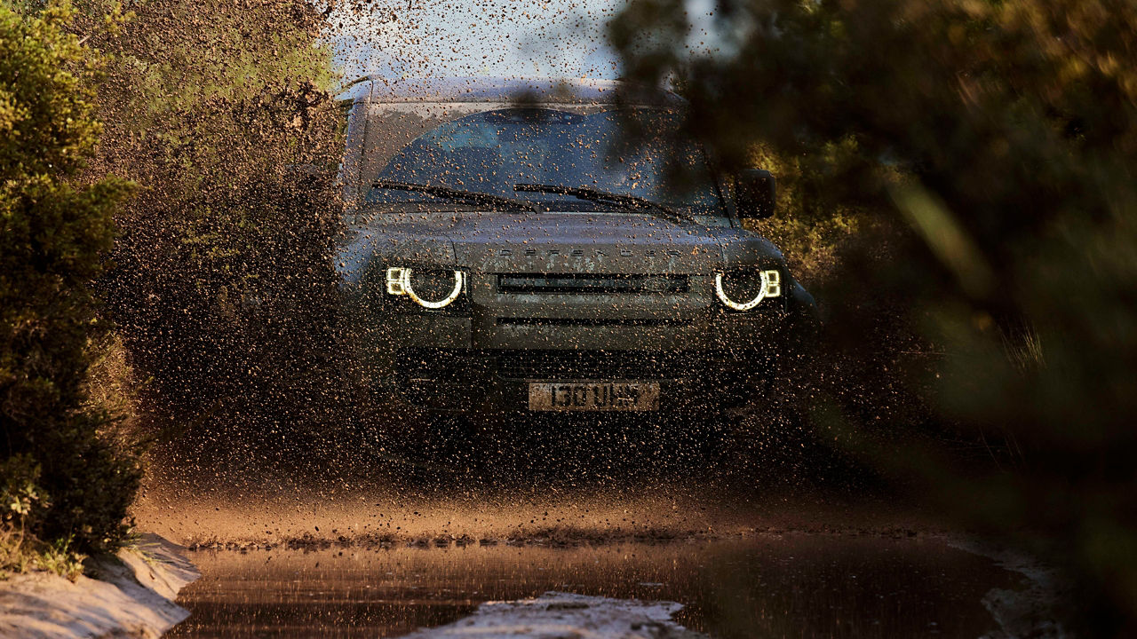 Defender driving through mud, with headlights shining.