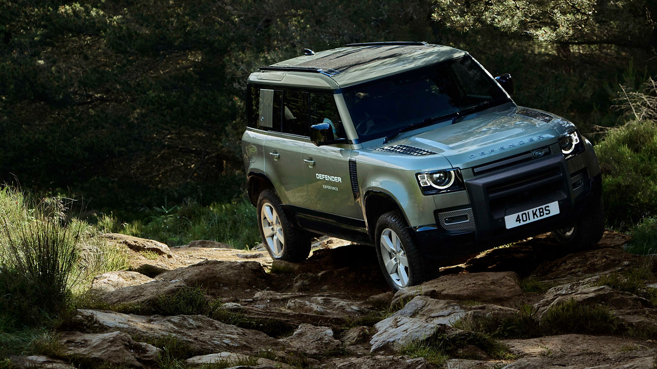 Defender driving over rocks in a forested area.