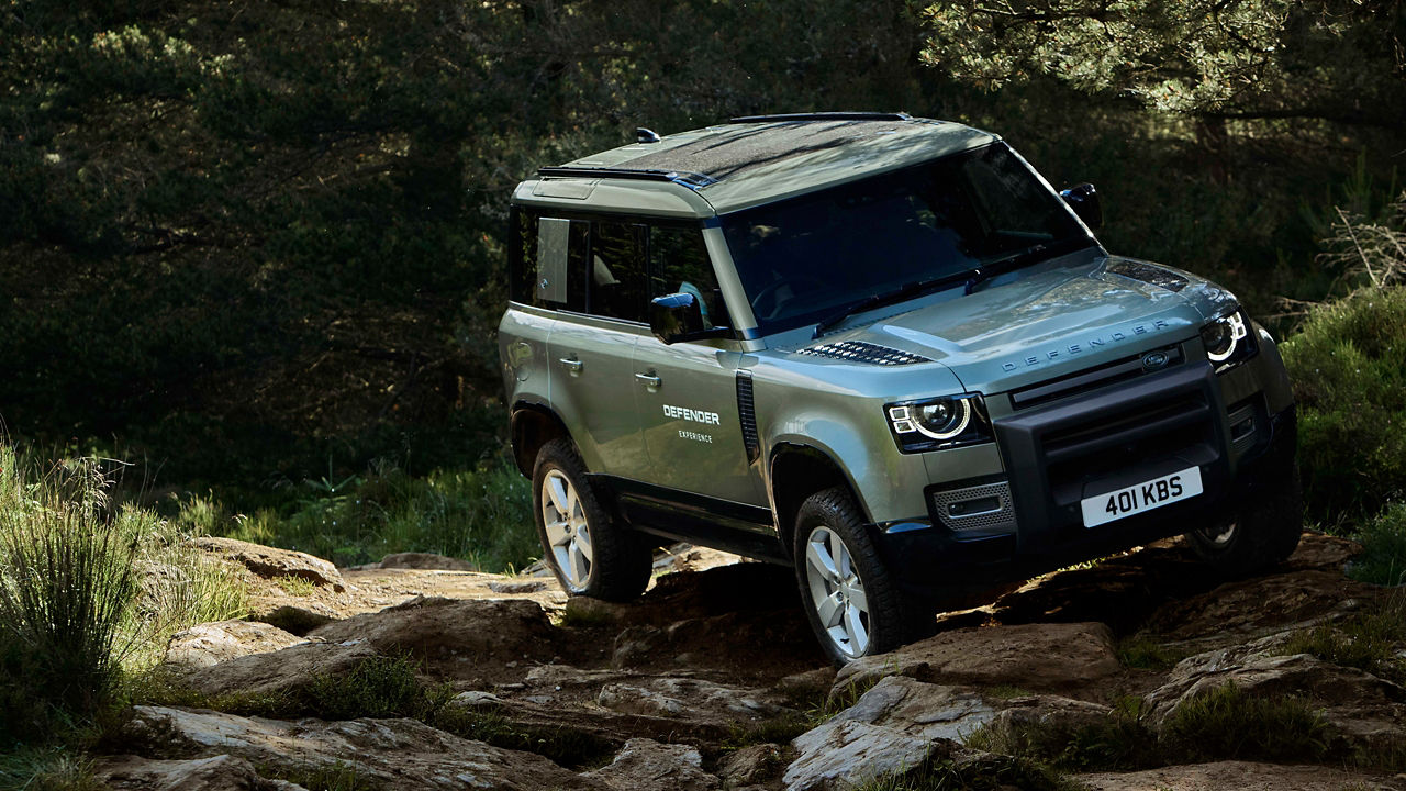 Defender driving over rocks in a forested area.