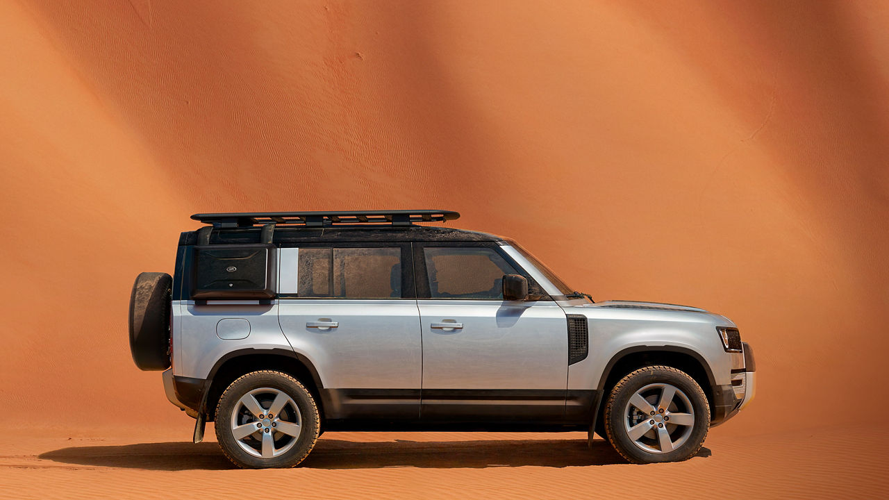 Side view of Defender 110 parked in a desert landscape with orange sand dunes.