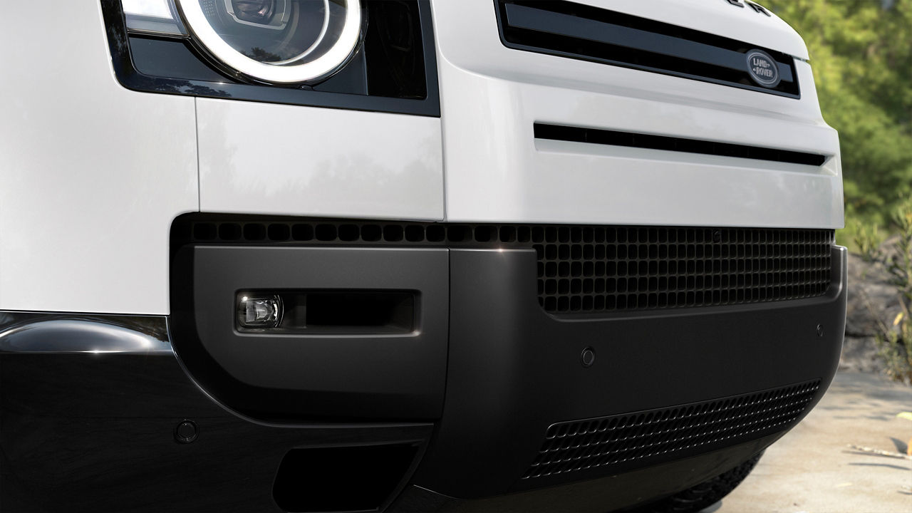 Close-up of the front bumper and headlight of a white Defender.