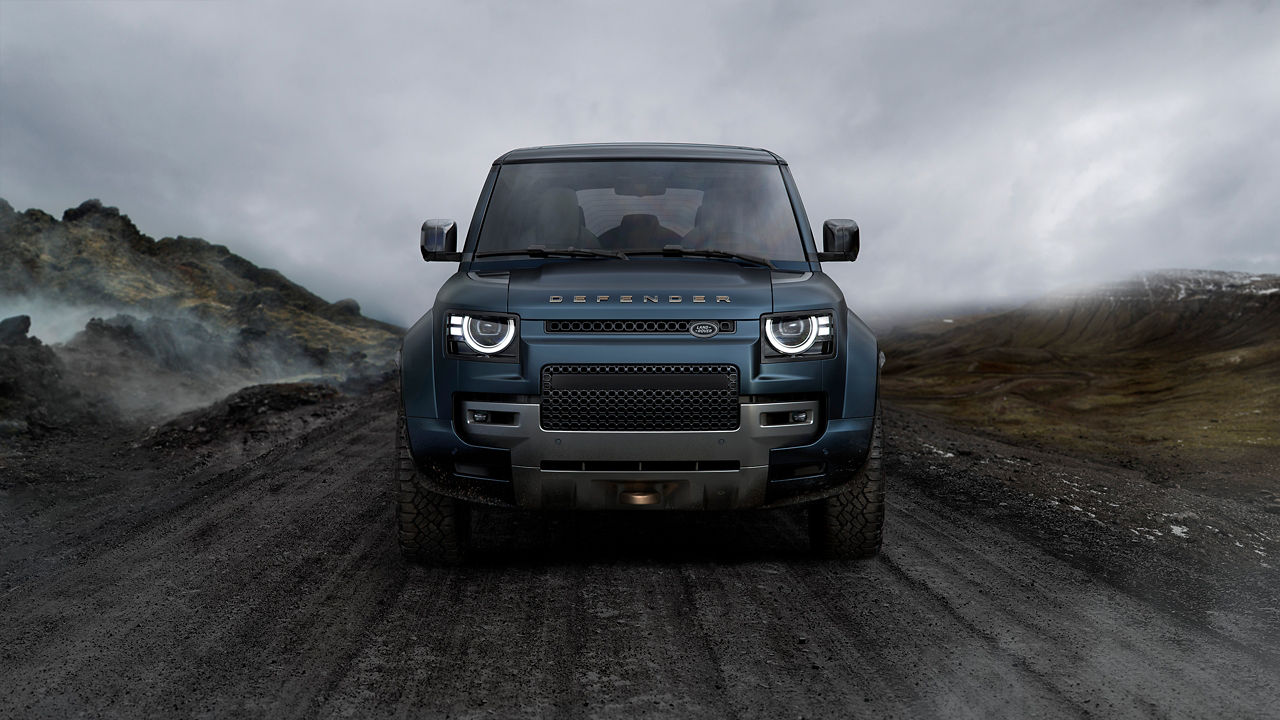 Front view of a blue Defender on a rugged mountain road under cloudy skies.