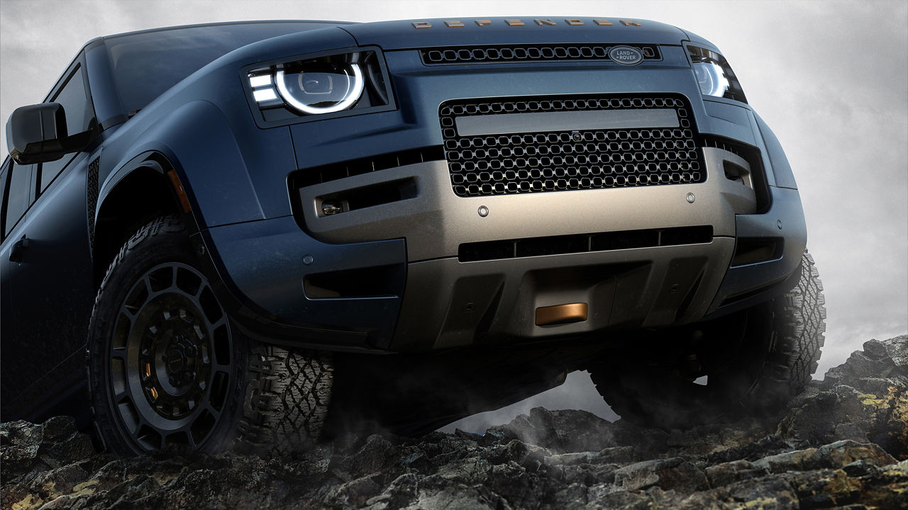 Low-angle front view of a blue Defender on rocky terrain.