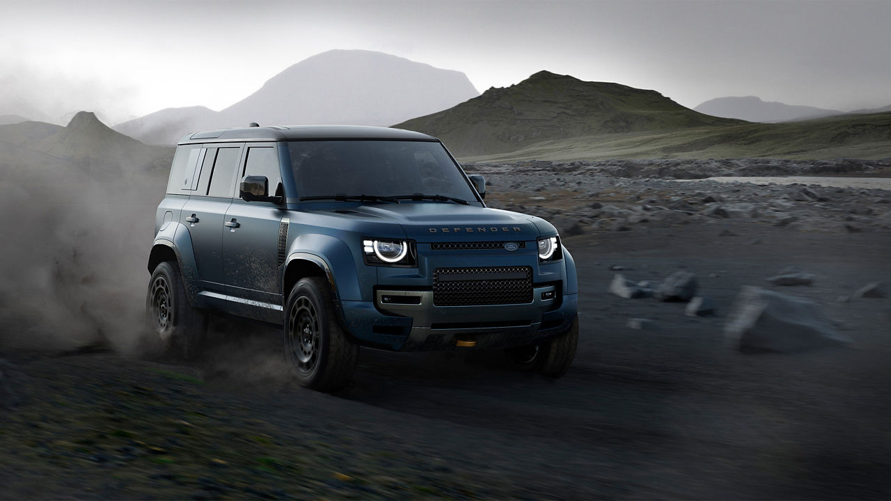 Blue Defender driving on a dirt road in a mountainous landscape.