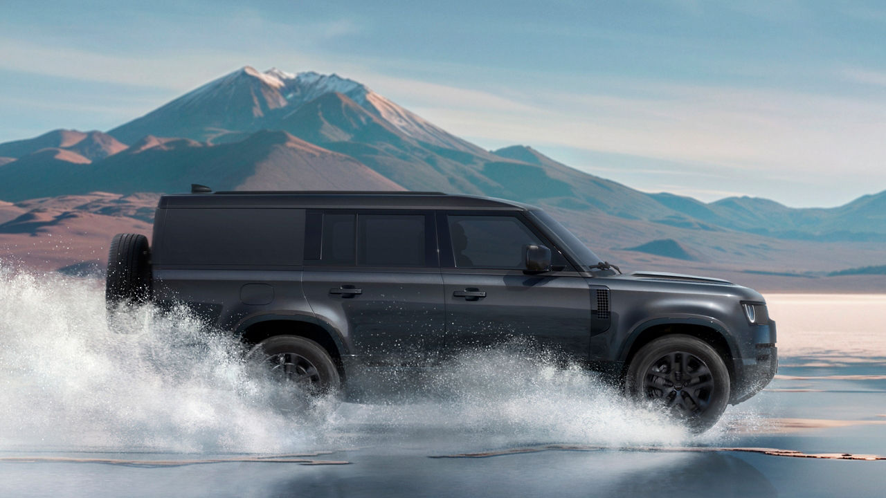 Defender crossing waterlogged road with large splashes