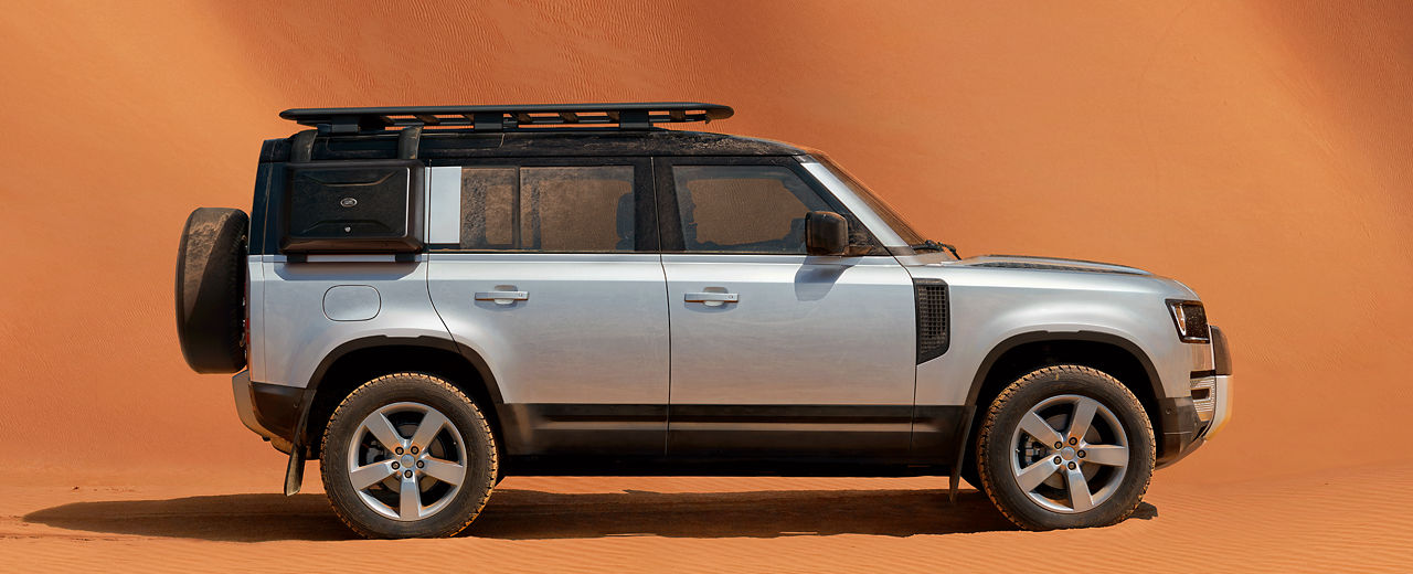 Side view of Defender 110 parked in a desert landscape with orange sand dunes.