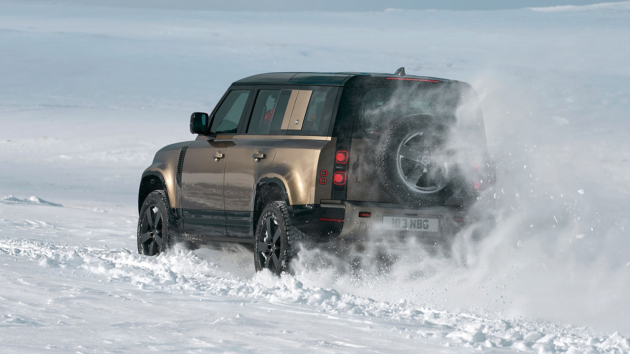 New Range Defender driving in snow back side view