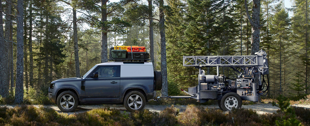 Defender 90 pulling a trailer through a path on a forest.