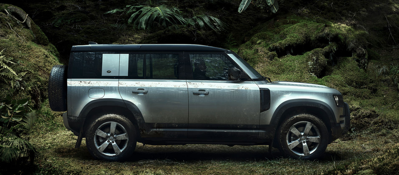 Side view of the Landrover Defender in a forestry setting with moss and shrubbery.