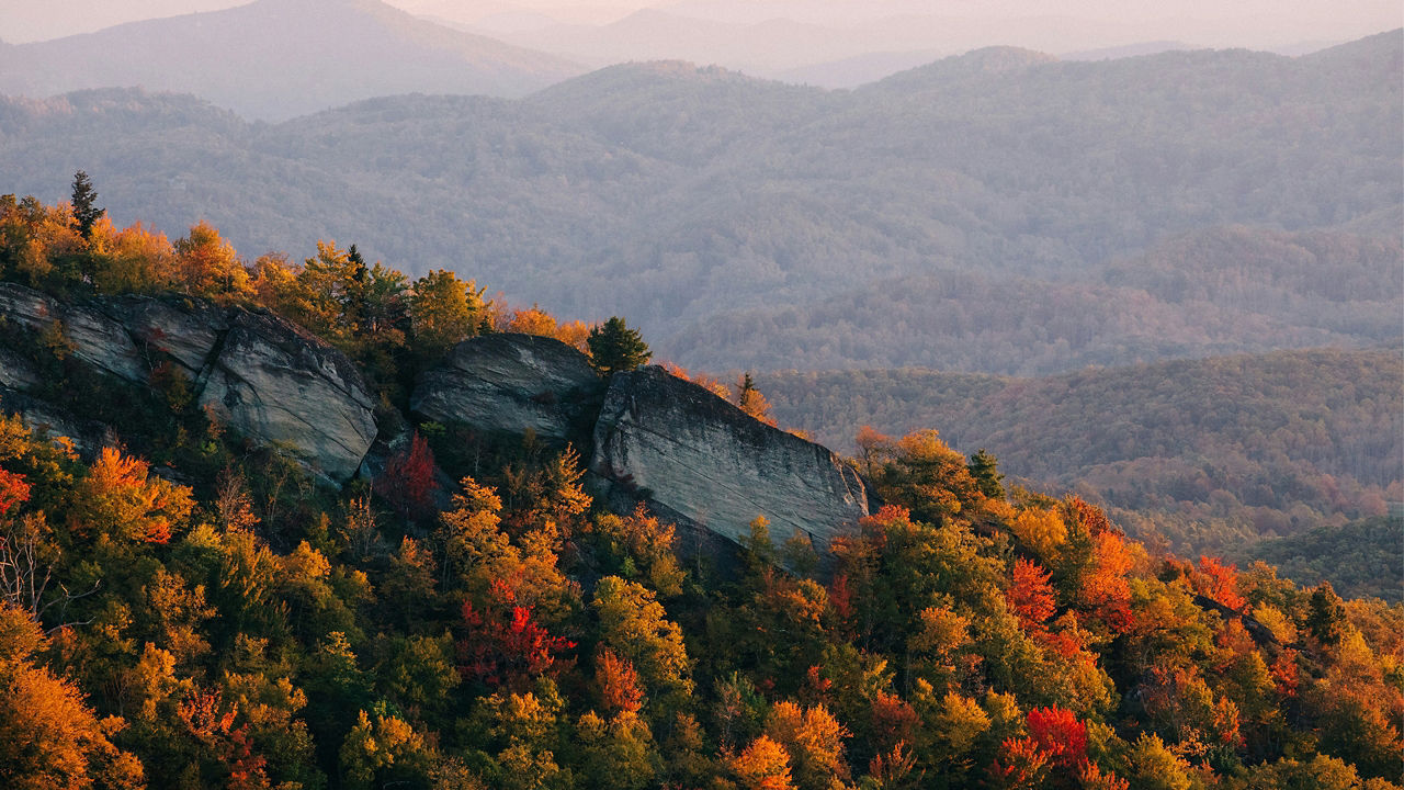 Rocky ridge with autumn trees overlooking distant hills.