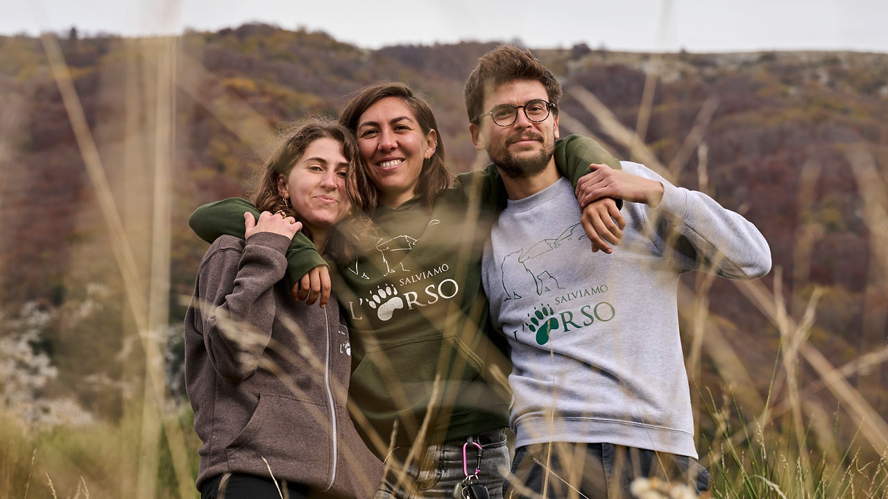 Three people standing together outdoors in a grassy, hilly landscape.