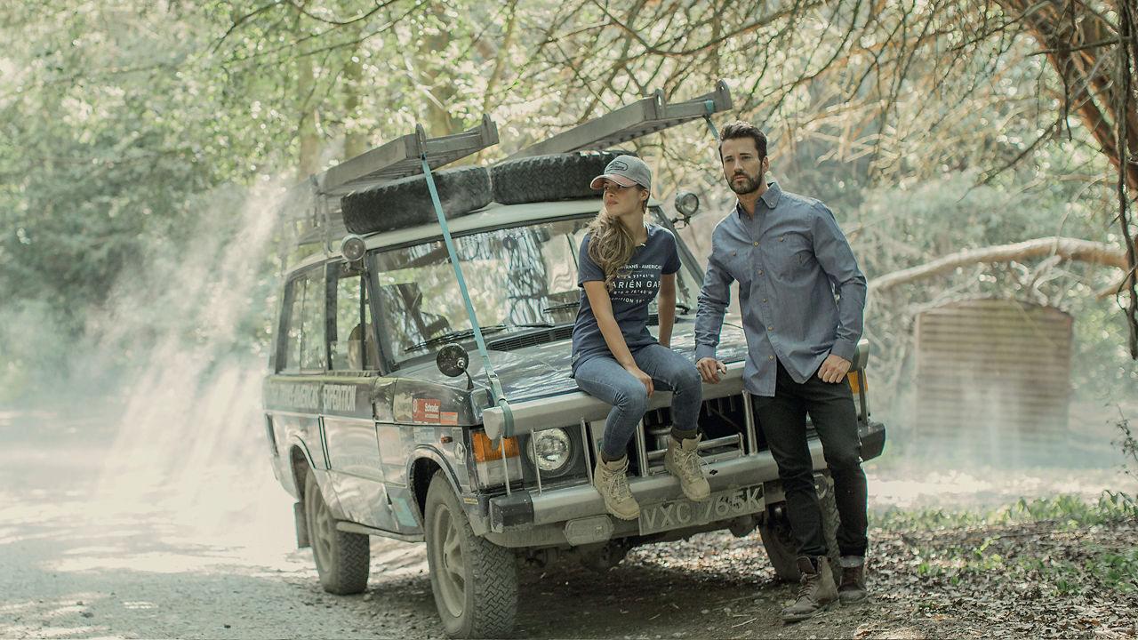 young couple looking and smiling while standing near their Defender car