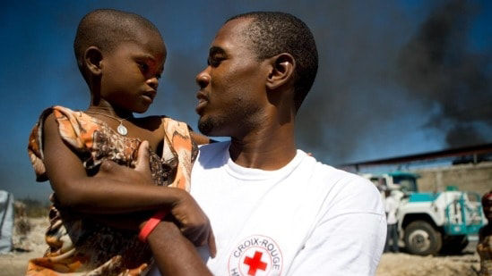 Man representing Red Cross holding young child 