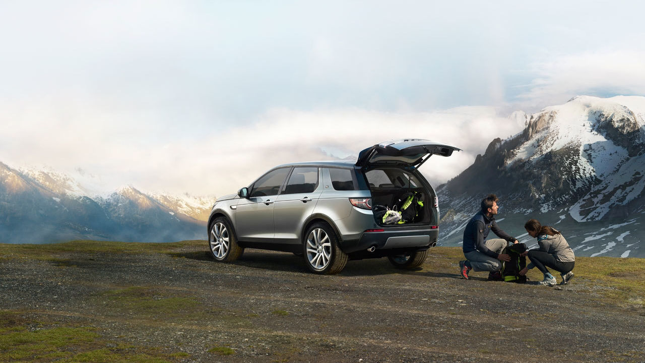 Range Rover with boot open and two people behind with Mountains surrounding