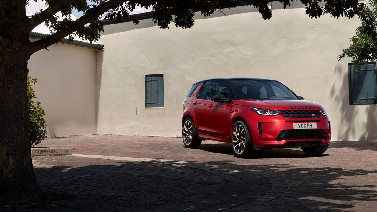 Red Discovery parked by tree and building